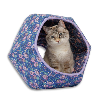 A tiny six-pound cat demonstrates our Cat Ball® cat bed made with a floral cotton fabric in blue, aqua, purple, and pink. Our hexagonal cat cave design has two openings and is flexible, lightweight, and made in the USA. 